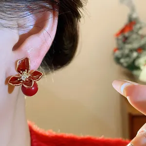 Detailed close-up of red resin flower stud earrings with pearls and golden trim