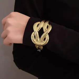 Close-up detail of a chunky gold-tone horseshoe knot bracelet worn over a black sleeve