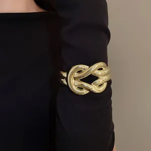 Detail of a chunky gold-tone interlocking knot cuff bracelet styled over a black sleeve.