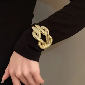 Close-up of a chunky gold horseshoe knot acrylic bracelet worn over a black sleeve