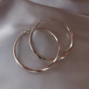 Elegant large silver hoop earrings with a flat twisted design on grey fabric background