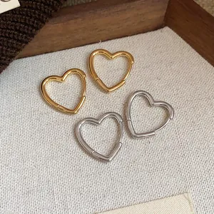 Detailed close-up view of minimalist gold and silver heart-shaped hoop earrings on textured fabric