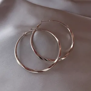 Detailed shot of large silver hoop earrings resting on a shimmering silk fabric surface.