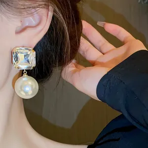 Close-up of elegant silver needle earrings with square crystal and large pearl drop