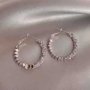 Close-up of silver hoop earrings with sparkling rhinestones on a silk background.