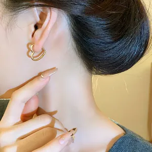 Detailed close-up showing a minimalist gold heart-shaped hoop earring worn by a model