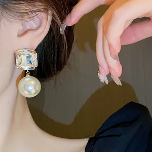 Detailed macro view of an elegant square crystal and pearl drop earring worn by a model