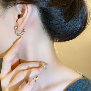 Close-up detail of a minimalist silver heart-shaped ear buckle earring worn on ear