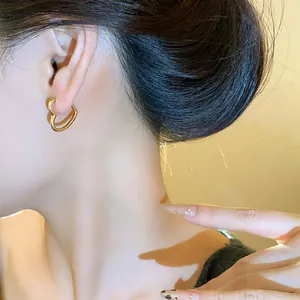 Detail shot of a minimalist gold heart-shaped hoop earring worn on a woman's earlobe