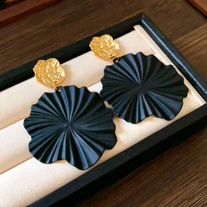 Macro detail of matte black mint leaf drop earrings with hammered gold textures