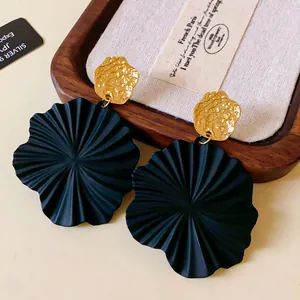 Close-up of black fan-shaped leaf earrings with gold textured tops on wooden tray