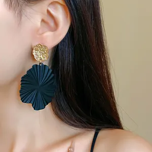 Detailed view of black pleated leaf earrings with gold accents worn by an Asian model