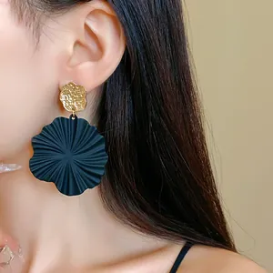 Close-up of black pleated leaf earring with gold textured stud on model's ear