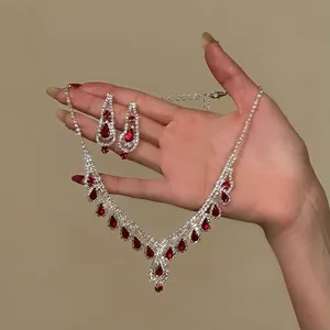 Detailed view of hand holding sparkling red teardrop crystal necklace and earrings set.