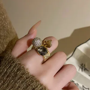Detail of gold-plated ring featuring a sparkling zircon sphere and dark gemstones.