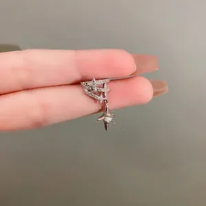 Sparkling zircon star ear cuff with dangling charm held by fingers for detail.