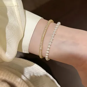 Elegant gold zircon mesh bangle paired with white pearl bracelet on wrist detail