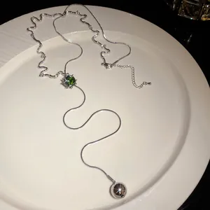 Detailed view of an elegant silver tassel necklace with a green zircon and metal ball