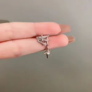 Detail view of a sparkling zircon star ear cuff held between fingers on grey background.