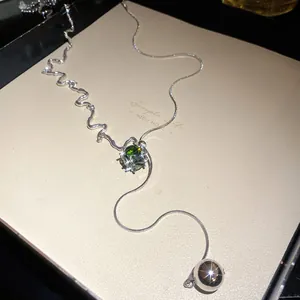 Close-up detail of a silver necklace featuring a square green zircon and wavy chain design