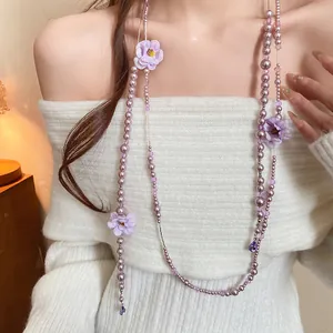 Detail of a long purple pearl necklace with fabric flowers and crystal beads.