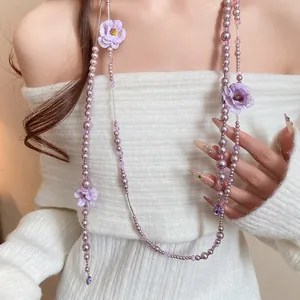 Close-up of purple pearl necklace with delicate fabric flowers and crystal accents.