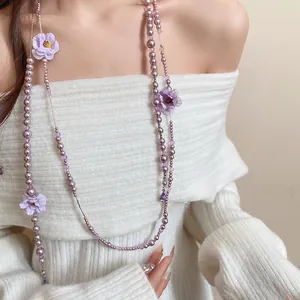 Detail view of a long purple pearl necklace with fabric flowers on a white knit sweater