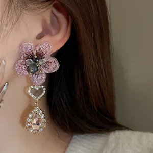 Détail de boucles d'oreilles fleurs brodées roses avec cristaux cœur et goutte.