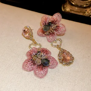 Gros plan sur des boucles d'oreilles asymétriques avec tissu floral rose et cristaux