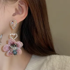 Gros plan détaillé d'une boucle d'oreille fleur en tissu rose avec cristaux de coeur