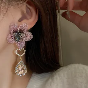 Gros plan détaillé d'une boucle d'oreille fleur brodée rose avec cœur en cristal