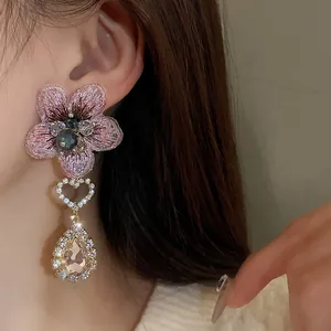 Gros plan d'une élégante boucle d'oreille fleur rose brodée avec cœur et cristal