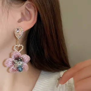 Gros plan de boucles d'oreilles fleur brodée rose avec cœur en cristal et goutte