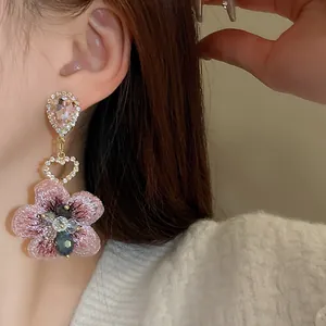 Gros plan d'une boucle d'oreille fleur en cristal rose avec un cœur en strass brillant.