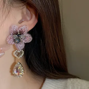 Détail d'une élégante boucle d'oreille fleur rose brodée avec cristaux pendants
