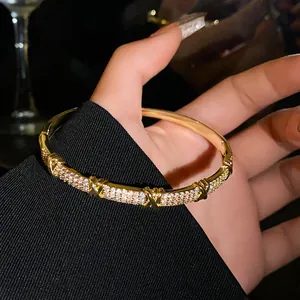Close-up of gold-plated bangle with pavé zircons and elegant X-shaped metal accents.