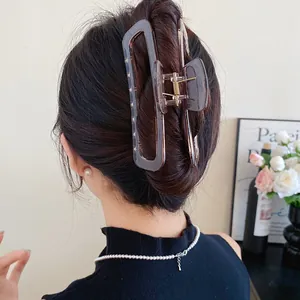 Gros plan détaillé d'une grande pince à cheveux en acrylique marron sur cheveux noirs.