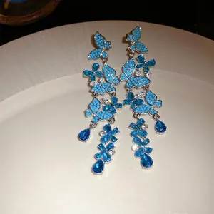 Elegant silver needle butterfly tassel earrings with blue rhinestones on a white plate