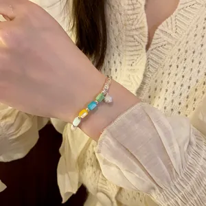 Detail of a colorful cylindrical bead elastic bracelet with a small flower charm.
