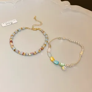 Detailed view of colorful cylindrical bead bracelets with silver and gold charms on a white tray