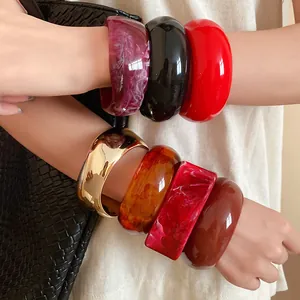 Detailed macro view of colorful chunky resin bangles and a polished gold cuff.