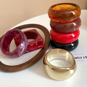 Detailed view of assorted geometric resin and gold chunky bangles on a wooden tray
