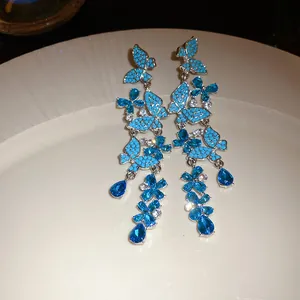 High detail view of elegant silver needle earrings with blue butterfly and flower crystals