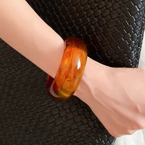 Close-up view of a thick amber resin open bangle worn on a wrist against a woven background