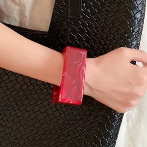 Close-up of a red marble-textured resin geometric bangle on a wrist against a black bag