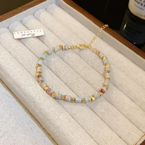 Close-up of a colorful cylindrical bead bracelet with gold accents on a velvet tray