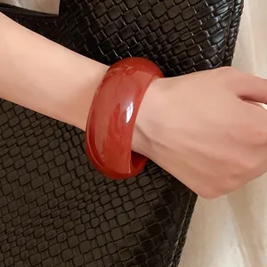 Close-up of a minimalist thick round resin bangle in reddish-brown worn on wrist
