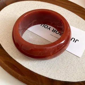 Macro view of a minimalist smooth red resin round geometric bangle on a rustic display tray