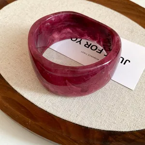Close-up detail of deep magenta resin bangle with elegant marble texture on a display card