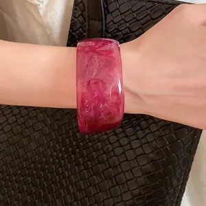 Detailed view of a stylish wide magenta marbled resin chunky bangle bracelet worn on a wrist